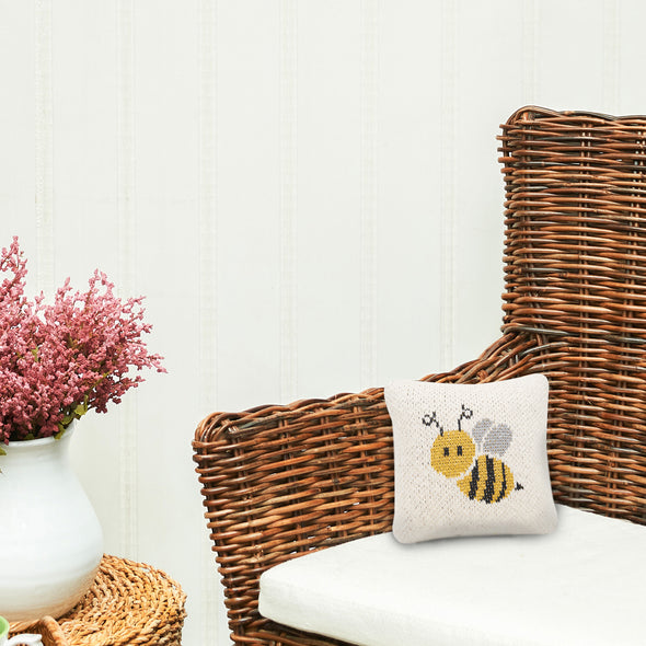 Bee knitted gift pillow with a neutral background and an adorable honeybee design on its front on a chair 