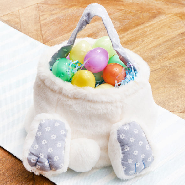 cotton tail bunny basket with two paws and a fluffy bunny tail. the handle and paws are light blue and have delicate white flowers. the basket is filled with easter eggs on a table