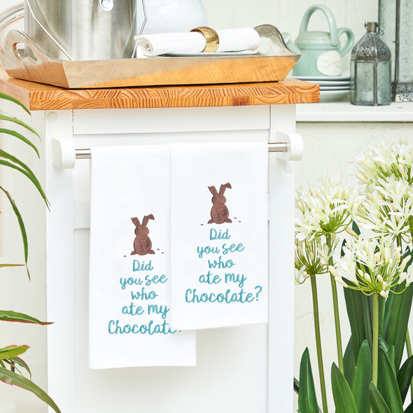 flour sack towel is the phrase Did you see who ate my chocolate below a chocolate bunny with bites taken from its ears. two of these towels are hanging from a counter