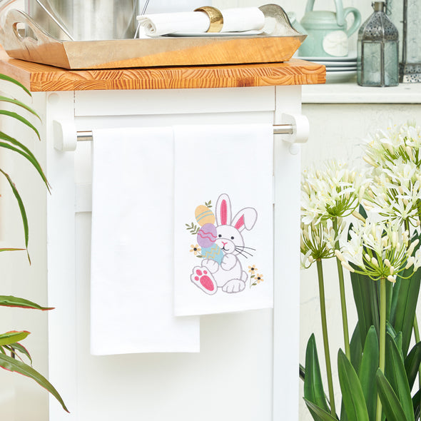 flour sack towel with an adorable bunny holding decorated easter eggs and surrounded by delicate flowers hanging from a kitchen counter