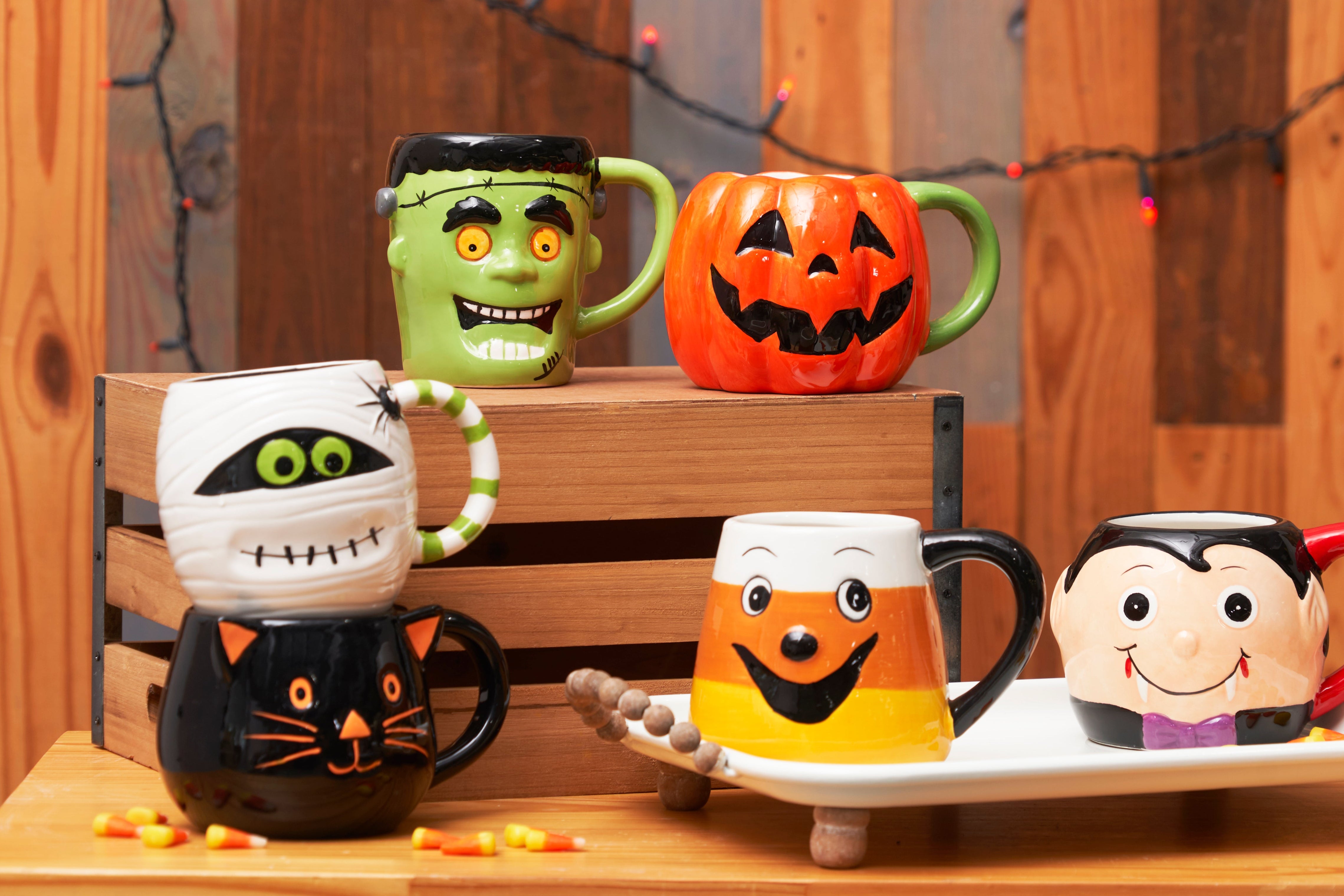 Set of Halloween-themed mugs on a wooden surface with decorative lights in the background.