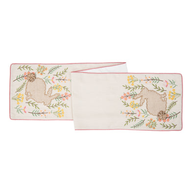 applique and embroidered runner with a natural background and natural and white bunny in the center surrounded by pink and yellow flowers and greenery. the pillow is trimmed in a coordinating pink.