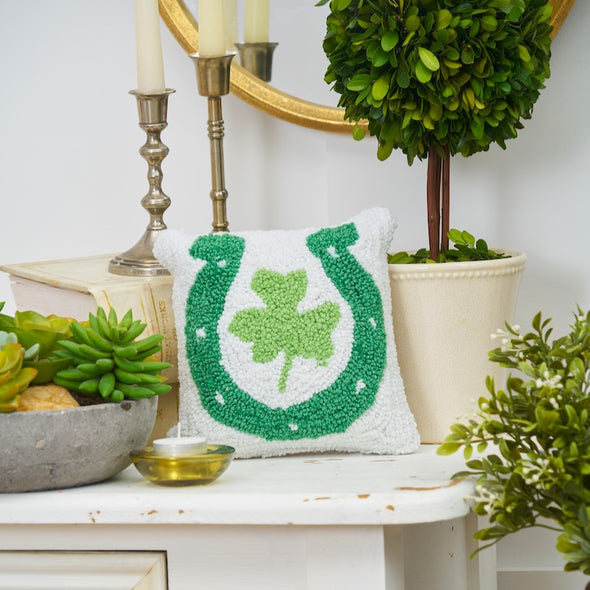 horseshoe clover mini hooked pillow on a table surrounded by plants