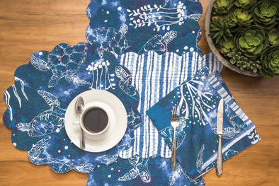 a variety of blues create a sea scape with turtles with a blue and white striped on the reverse side of the quilted placemat