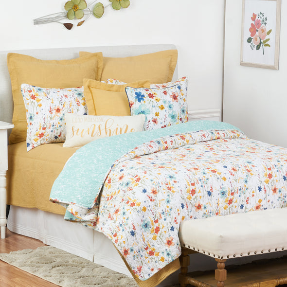 quilt with a watercolor inspired wildflower print in vibrant red, yellow, and blue flowers that reverses to a coordinating blue with an abstract foliage style print