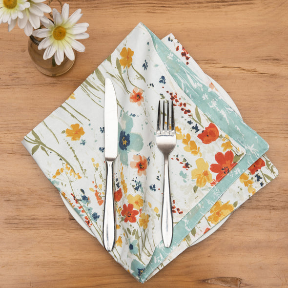 quilted table linens with a watercolor inspired pattern of wildflowers in bright colors including red, orange, and blue that reverses to a coordinating blue and a simple abstract foliage style pattern