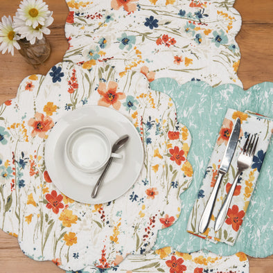 quilted table linens with a watercolor inspired pattern of wildflowers in bright colors including red, orange, and blue that reverses to a coordinating blue and a simple abstract foliage style pattern