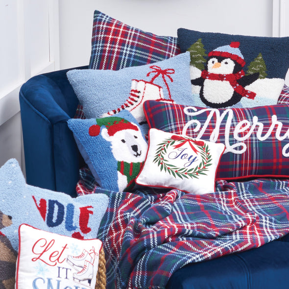 hooked pillow with a penguin dressed in winter clothing ice skating in the wintertime surrounded by additional winter and Christmas themed home decor on a blue chair