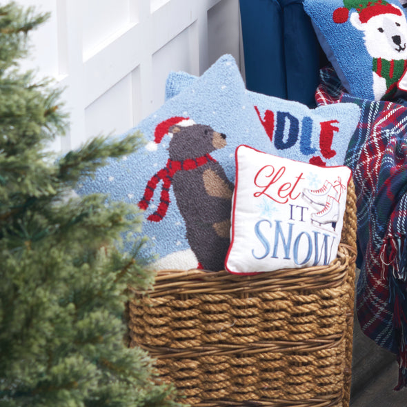 hooked pillow depicting a brown bear wearing a red hat and scarf sledding down a snowy hill on a red sled in a basket with other winter and Christmas home decor