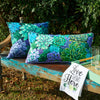pillow with vibrant green blue and purple succulents on a black background paired with a love grows here kitchen towel on an outdoor bench