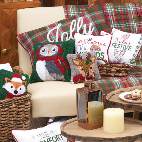 hooked pillow depicting an owl wearing earmuffs and a scarf on a green background surrounded by additional Christmas decor on a sofa