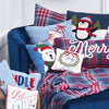 hooked pillow depicting a white polar bear wearing a red and green hat and scarf on a light blue background surrounded by additional winter Christmas decor on a blue chair