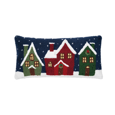 hooked pillow depicting a village with snow-covered rooftops. the houses are decorated for Christmas with wreaths as snow falls in the background