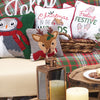 hooked pillow with a reindeer wearing a red scarf with a holly berry and leaf in its antler on a grey background on a couch surrounded by additional winter and Christmas decor