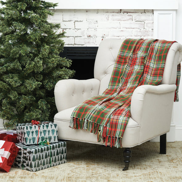 woven plaid throw with a forest green red and yellow design and tassel edges on a chair next to a tree and presents