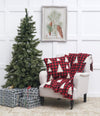 knitted throw with a red and black buffalo check pattern with white trees and a matching pillow on a chair next to a tree and presents