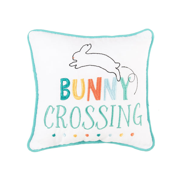 With a sweet Easter design embroidered in a colorful palette of teals, orange, and yellow, as well as the words "Bunny Crossing". Finished with a teal piped border and a bunny figure jumping over the words