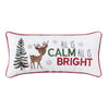 white pillow embroidered with the phrase all is calm all is bright next to an adorable reindeer and decorated Christmas tree surrounded by silver snowflakes. the pillow is trimmed in red