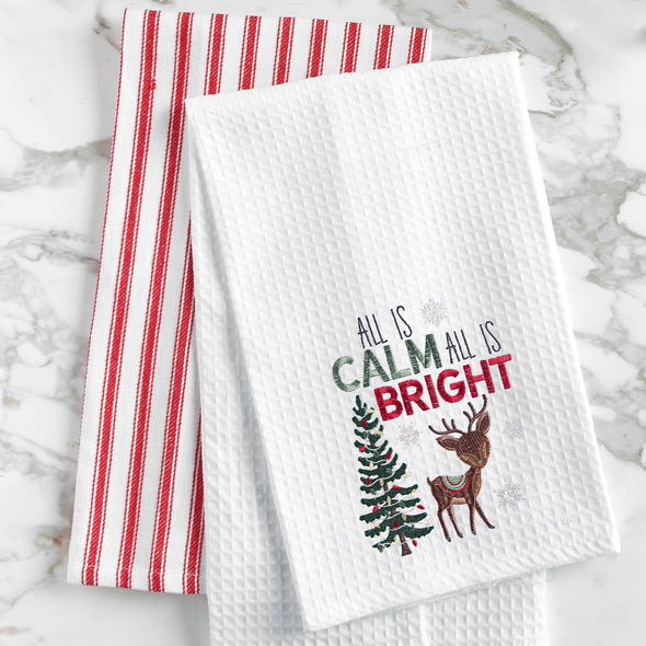 waffle weave towel with the phrase All is Calm All is Bright above an adorable reindeer next to a decorated Christmas tree on a marble countertop