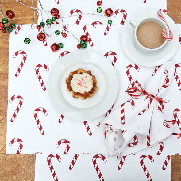 printed table linens with red and white candy canes on a white background on a wood table with cocoa and holiday decor