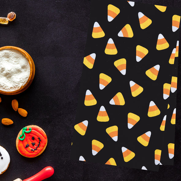 black printed flour sack towel with a scattered repeating design of candy corn pieces next to Halloween candy