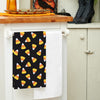 black printed flour sack towel with a scattered repeating design of candy corn pieces hanging from a kitchen counter