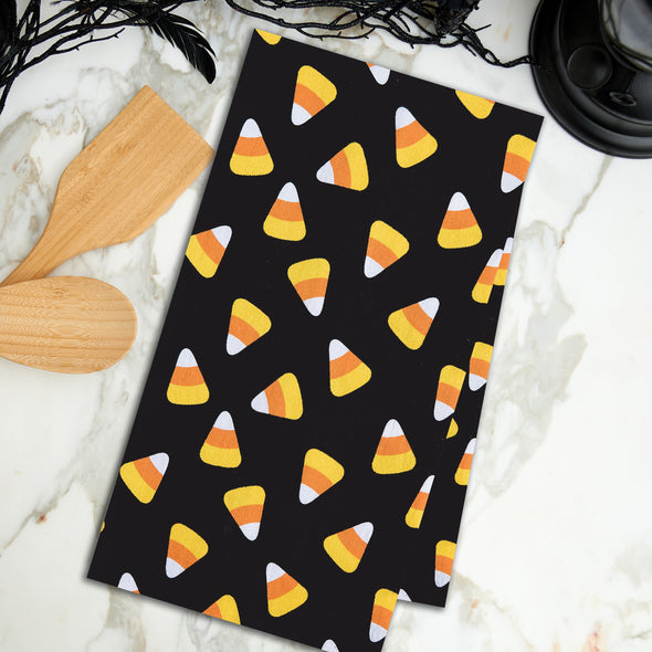 black printed flour sack towel with a scattered repeating design of candy corn pieces on a marble countertop