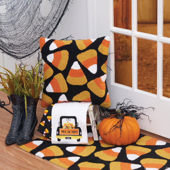 black hooked pillow with orange yellow and white candy corn pieces scattered in an all over pattern surrounded by Halloween decor