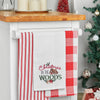 a waffle weave towel with a log cabin surrounded by the words Christmas in the woods in different scripts and decorated with holly berries and flowers hanging from a kitchen countertop