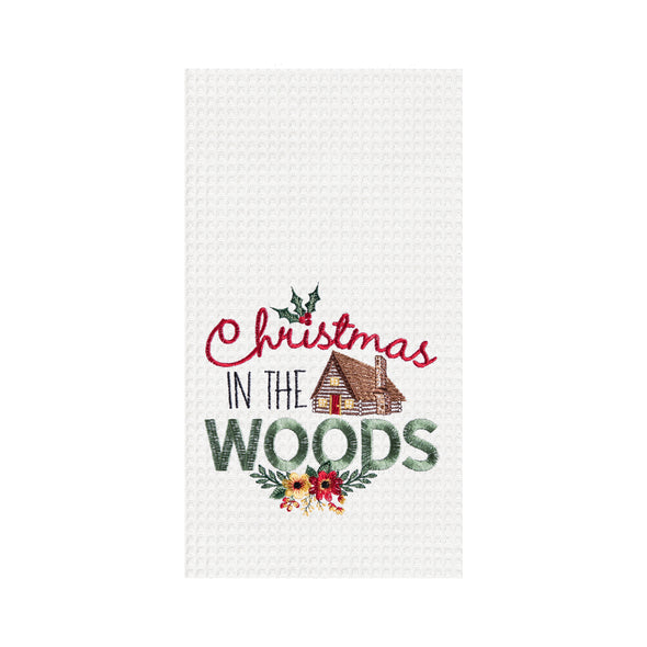 a waffle weave towel with a log cabin surrounded by the words Christmas in the woods in different scripts and decorated with holly berries and flowers