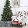 knitted throw with green christmas trees and trimmed in red on a chair next to a tree and presents