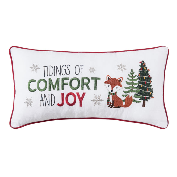 white pillow with the phrase tidings of comfort and joy embroidered next to an adorable fox and decorated Christmas tree. the pillow is trimmed in red