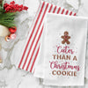 embroidered flour sack towel with a gingerbread man cookie on top and the phrase cuter than a Christmas cookie below in different fonts on a marble countertop