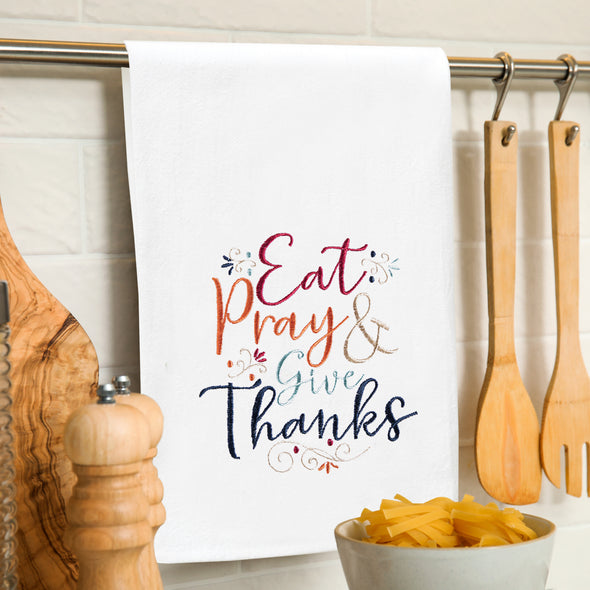 flour sack towel with the phrase Eat Pray & Give Thanks in inviting Autumn colors and a delicate script highlighted by flourishes hanging from a towel bar in the kitchen