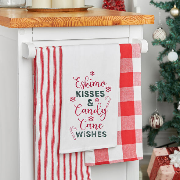 embroidered flour sack towel with the phrase eskimo kisss and candy cane wishes surrounded by snowflakes and candy canes hanging from a kitchen counter