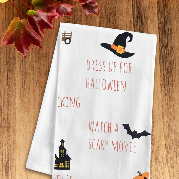 printed flour sack towel with an illustrated fall bucket list including all the activities you can do in the fall on a wood table with fall foliage