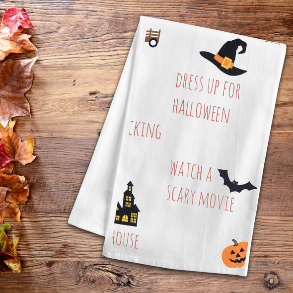 printed flour sack towel with an illustrated fall bucket list including all the activities you can do in the fall on a wood table with fall foliage