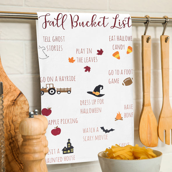 printed flour sack towel with an illustrated fall bucket list including all the activities you can do in the fall hanging from a towel bar in a kitchen