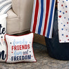 embroidered gift pillow with the words family friends fun and freedom embroidered surrounded by blue light blue and red stars and trimmed in red next to a couch covered in additional patriotic decor