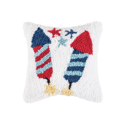 a white hooked pillow with two brightly colored fire crackers in patriotic colors as well as yellow sparkles resembling a firecracker igniting