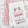 embroidered flour sack towel with the phrase gingerbread kisses and Christmas wishes below a gingerbread man and gingerbread woman on a marble countertop