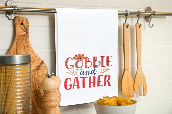 Embroidered Gobble and Gather kitchen towel hung on a kitchen utensil bar.