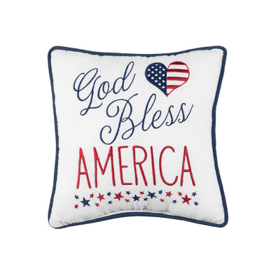 an embroidered pillow with the words God bless America in various font styles and underscored with tiny red and blue stars. a heart resembling the stars and stripes of the American flag complements the design.