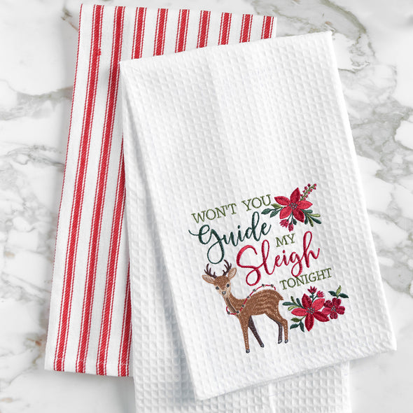 waffle weave towel with the phrase won't you guide my sleigh tonight in different font styles nestled between an adorable reindeer and red flower arrangements on a marble countertop