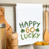 embroidered waffle weave towel with the words Happy Go Lucky surrounded by two clovers hanging on a kitchen towel rack