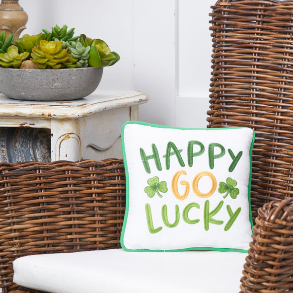 embroidered mini gift pillow with the words happy go lucky on a white background next to green clovers on a wicker chair