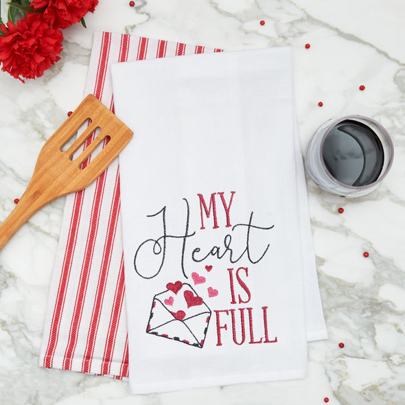 embroidered flour sack towel with the phrase my heart is full next to a letter bursting with pink hearts on a marble kitchen counter