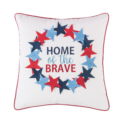 an embroidered and applique pillow with a wreath of red and blue stars surrounded the phrase home of the brave. the pillow is trimmed in red