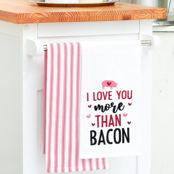 flour sack towel with the phrase I love you more than bacon surrounded by pink and red hearts hanging from a kitchen counter