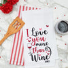 flour sack kitchen towel with an embroidered phrase of I love you more than wine surrounded by little hearts on a marble counter